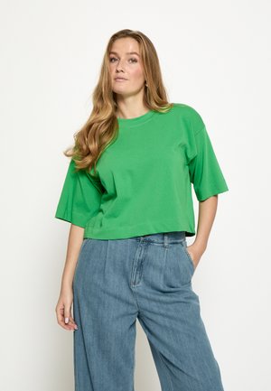 Grøn cropped t-shirt i blødt stof med rund halsudskæring og korte ærmer, kombineret med løstsiddende lyseblå denimbukser.
