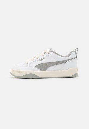 Hvid og grå Puma lavtop sneaker med beige sål, grå Puma-stribe, hvide snørebånd og hæl trækstrop på en ensartet lys baggrund.