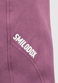 Ropa deportiva de algodón morado con superficie texturizada y un logotipo bordado "SMILODOX" en blanco en el lateral.
