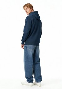 Felpa con cappuccio blu navy dal taglio rilassato, abbinata a jeans baggy blu chiaro e sneakers bianche, caratterizzata da un design semplice e una texture morbida.