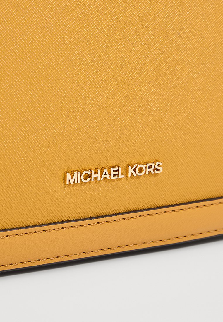 Gelbes strukturiertes synthetisches Leder mit sichtbaren Nähten und einem goldfarbenen, eingeprägten "MICHAEL KORS"-Logo auf der Oberfläche.