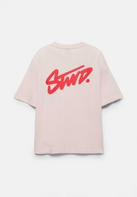 T-shirt rose clair à manches courtes avec une coupe oversize et un texte rouge vif stylisé "Stwd." imprimé sur le haut du dos.