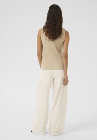 Beige ribbad ärmlös topp i kombination med krämf�ärgade vida byxor, båda med mjuka texturer och avslappnad passform. Minimalistisk design utan mönster.