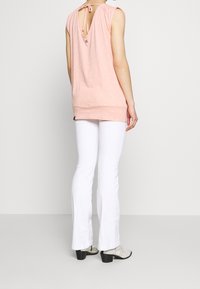 Top senza maniche di un rosa chiaro con pois bianchi, con uno scollo sulla schiena e un dettaglio con fiocco. Abbinato a pantaloni a zampa bianchi e calzature texturate.