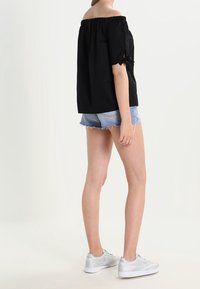 Top nero scollato con spalle scoperte e maniche corte, abbinato a pantaloni corti di jeans e sneakers argento. Design semplice con una vestibilità comoda.