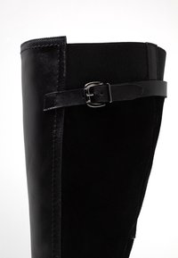 Czarne kozaki do kolan wykonane z materiału skórzanego i elastycznego, o gładkiej fakturze, z boczną taśmą z detalem w postaci srebrnej klamry.