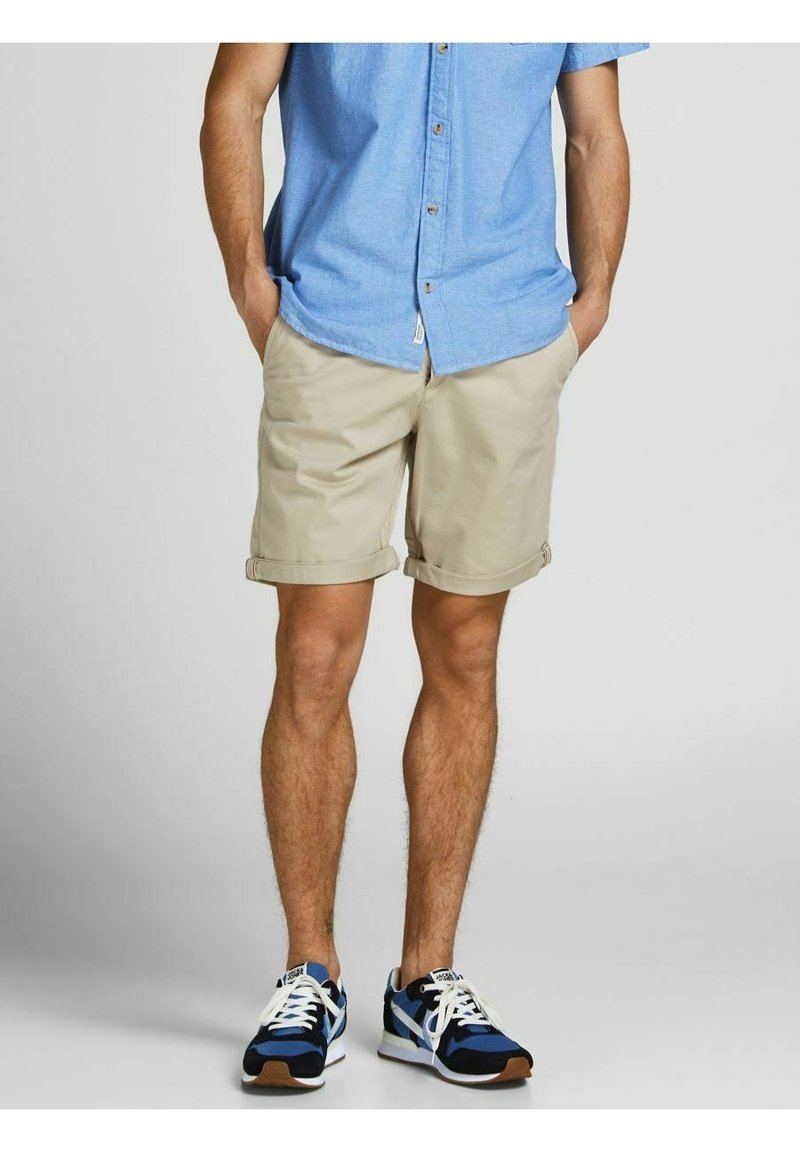 Light blue button-up shirt, beige rolled-up shorts, and blue sneakers with black accents. Casual outfit with varied textures and colors.