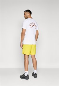White t-shirt with "Giddy Up" text in dark orange on the back, paired with bright yellow shorts and black sneakers.