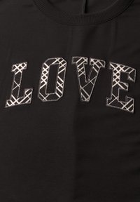 Tissu noir avec le mot LOVE brodé en grandes lettres majuscules présentant des motifs croisés blancs et gris.