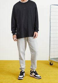 Svart långärmad Nike t-shirt, grå sweatpants och svart-vita träningsskor. Enkelt mönster, avslappnad passform och mjuka tygtexturer.