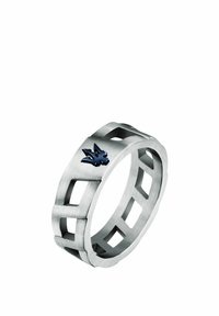 Anello in metallo tono argento con motivi geometrici ritagliati e un accento logo nero. La superficie presenta una finitura spazzolata.