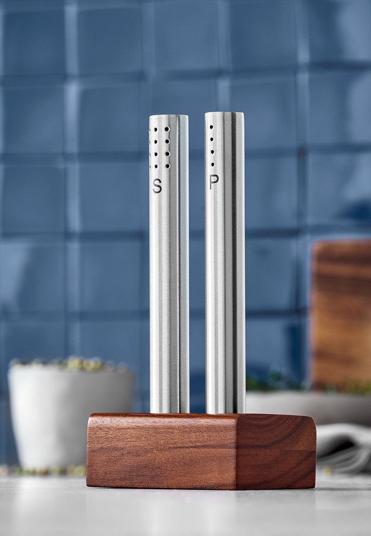 Saliera e pepiera in acciaio inox con coperchi perforati, etichettati "S" e "P", poggiate su un portaraccoglitore in legno marrone.
