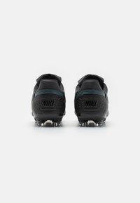 Crampons Nike noires avec une finition texturée, doté d'un accent vert le long du talon et de crampons translucides à la semelle. Logo en relief à l'arrière.