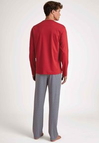 Un haut de pyjama rouge à manches longues associé à un pantalon ample à motifs bleu et blanc avec un design en losanges.