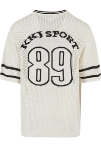 Krémový pletený top s krátkým rukávem, který obsahuje černou síťovanou strukturu, nápis "KJS SPORT" a grafiku "89" na zadní straně s kontrastními pruhy.
