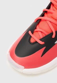Helle rote und schwarze Sportschuh mit pinken Schnürsenkeln, Obermaterial aus Netzgewebe und weißer Sohle, präsentiert auf einem einfachen hellen Hintergrund.