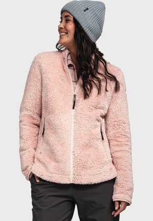 Roze nepbont jasje met een rits, zijzakken en een zachte textuur. Gemos met een lichtgrijze beanie, gedragen met donkere broeken.