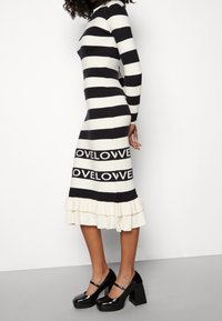 Raidallinen neulemekko mustavalkoisena, jossa on ripsureuna ja "LOVE" -tekstisuunnittelu keskikohdassa. Yhdistetty mustien korkojen kanssa.