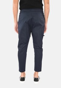 Pantaloni blu navy con un elastico in vita, dalla vestibilità slim e gambe affusolate. Il tessuto appare leggero con una superficie liscia e cuciture rinforzate.
