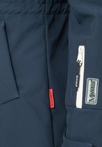 Navy outdoor jacket featuring a textured fabric, white zip pocket, side flap pocket, and a prominent red brand tag.