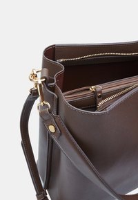Borsa a tracolla in ecopelle marrone con hardware dorato, diversi scomparti con zip e una tracolla removibile. Superficie esterna testurizzata.