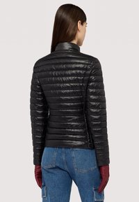 Černá prošívaná péřová bunda s úzkým střihem, vysokým límcem a lesklou texturou. Doplněno červenými koženými rukavicemi a modrými džínovými kalhotami.