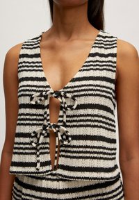 Schwarz-weißer gestreifter ärmelloser Oberteil mit tiefem V-Ausschnitt und Bindeschluss-Detail. Hergestellt aus strukturiertem Strickmaterial.
