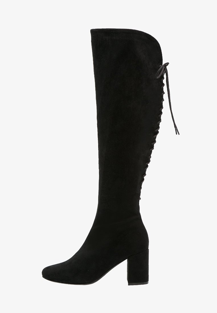Stivale sopra il ginocchio in suede nero con tacco a blocco, caratterizzato da una parte superiore curva e dettagli con lacci lungo il lato esterno.
