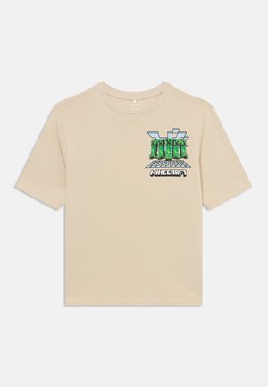 Béžové bavlněné tričko s krátkým rukávem, které má na přední straně barevnou grafiku z Minecraftu. Má kulatý výstřih, volný střih a hladkou texturu.