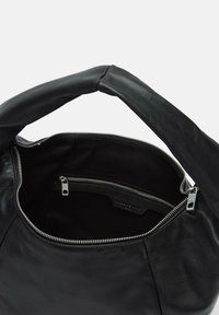 Czarna skórzana torebka o miękkiej fakturze, z zamkiem błyskawicznym i wewnętrzną kieszenią; posiada zaokrągloną rączkę ułatwiającą noszenie.
