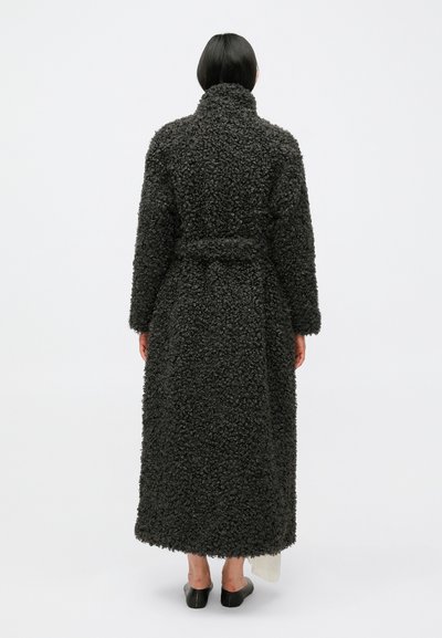 Dugi, tamnosivi kaput od teksturiranog, vunenog materijala s visokim ovratnikom, remenom u struku i širokim krojem.