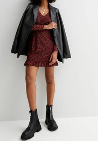Schwarze Lederblazer über einem roten, blumigen Kleid mit Rüschensaum, kombiniert mit klobigen schwarzen Knöchelstiefeln mit Reißverschluss.