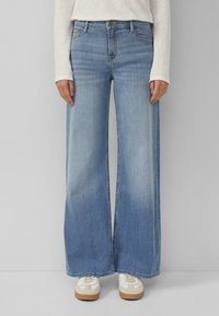 Szerokie dżinsy w kolorze niebieskim wykonane z denimu, z wysokim stanem i delikatnym spraniem. Do tego białe trampki z wielowarstwową podeszwą.