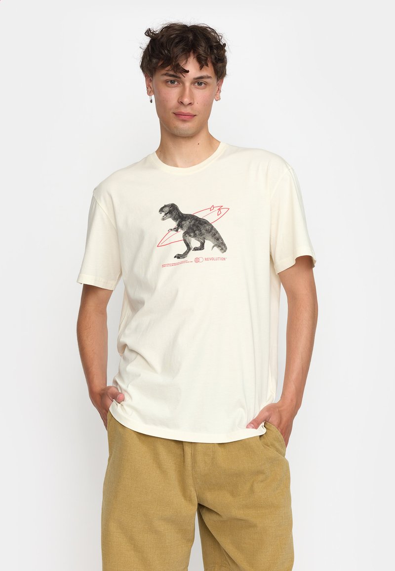 Crème t-shirt van katoen, met een zwart dinosaurussymbool met rode accenten. Model staat met de handen in de zakken en draagt een beige short.
