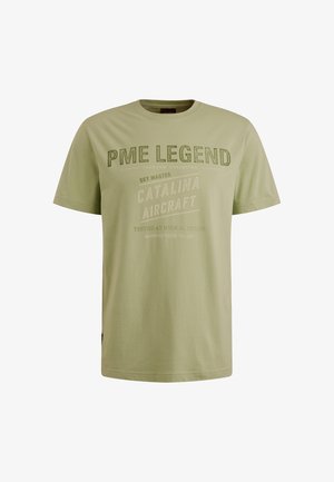 Camiseta de algodón verde oliva claro con mangas cortas, que presenta texto impreso en diferentes fuentes y tamaños en el pecho y la parte superior del cuerpo.