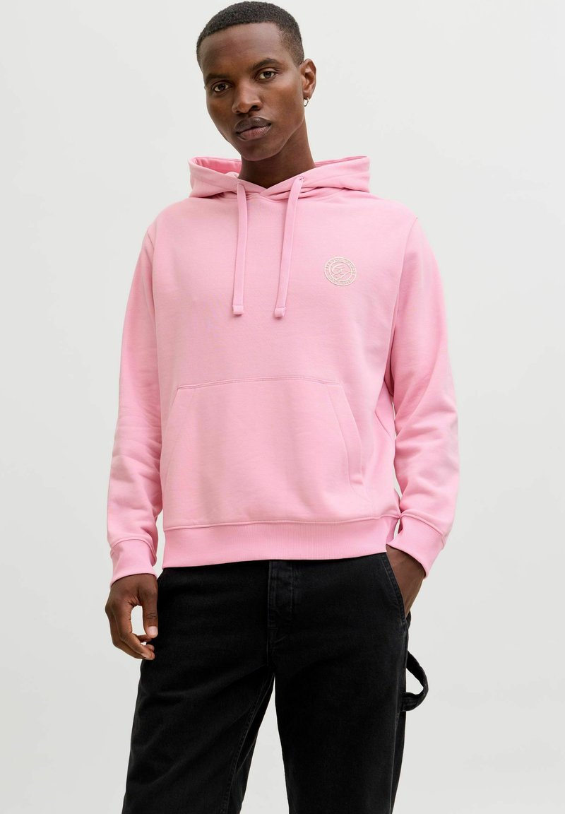 Hoodie rose clair avec une poche avant, une capuche à cordon et un petit détail de logo. Fabriqué en tissu doux avec une texture lisse. Assorti à un pantalon noir.