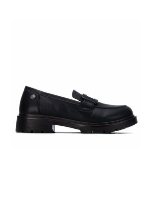 Mocasín de cuero negro con suela gruesa, puntera redonda, detalle de correa en la parte superior y un pequeño emblema metálico redondo cerca del talón.