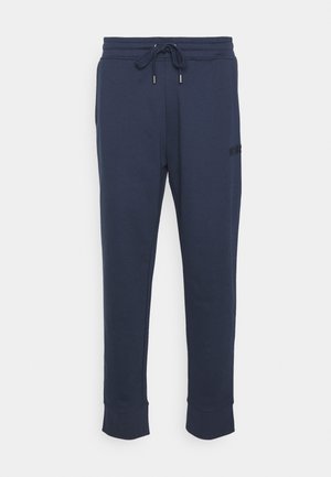 Marineblå joggingbukser med snøre i taljen og manchetter ved anklerne, med diskrete sidelommer og et lille syet logo på låret.