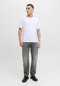 Tricou alb din bumbac asortat cu blugi gri deschis, cu croială dreaptă. Pantofi negri completează ținuta. Design simplu și casual, fără modele vizibile.