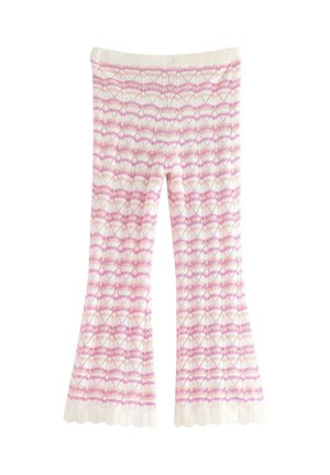 Ung pige står iført matchende lyserødt og hvidt mønstret striktop og bukser med bølgede kanter samt lyserøde sandaler med sløjfer.