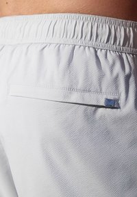 Weiße Sportshorts aus strukturiertem Stoff, mit elastischem Bund und einer Gesäßtasche, die mit einem kleinen blauen Logoakzent versehen ist.