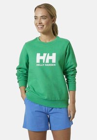 Sudadera verde con un logo blanco de "Helly Hansen", cuello redondo, puños y dobladillo de canalé. Combinada con pantalones cortos de un azul claro para crear contraste.