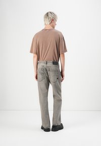 Jeans din denim gri cu o croială lejeră, având un design al buzunarului din spate și un eticheta neagră în contrast. Asortați cu un tricou maro, cu o croială lejeră.