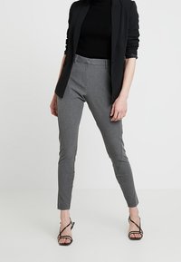 Pantalons gris ajustés avec une coupe slim et un tissu texturé, associés à un haut noir et un blazer noir. Des escarpins noirs à brides complètent la tenue.