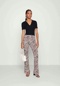Top preto de manga curta com decote em V, combinado com calças largas em estampado de zebra castanho e branco. Acessórios incluem uma mala branca e saltos pretos.