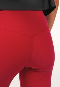 Leggings rossi a vita alta realizzati in tessuto elasticizzato, con cuciture piatte e una texture liscia, progettati per comfort e flessibilità.