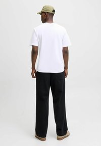 T-shirt en coton blanc à manches courtes, associé à un pantalon noir ample. Une casquette vert olive clair avec une sangle sombre complète le look.