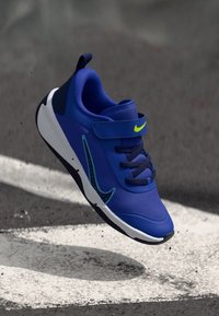 Chaussure de sport bleue avec une tige en maille et une fermeture par sangle. Comprend des accents vert fluo, une semelle texturée et un design épuré.