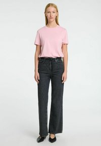 Camiseta de manga corta rosa combinada con vaqueros de pierna ancha negros de cintura alta y zapatos planos negros, con un ajuste relajado y silueta recta.