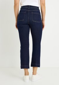 Pantalones vaqueros de mezclilla azul oscuro con cintura alta, corte recto y costuras amarillas contrastantes. Presentan dos bolsillos traseros y longitud recortada.